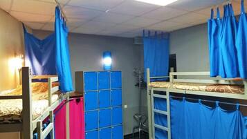 Un dormitorio con literas, una cortina azul, un armario y un taburete pequeño.