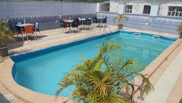 A rectangular swimming pool with a tiled edge, surrounded by a tiled patio area with outdoor seating. - Fatty K Hotel and Suites (Ota)