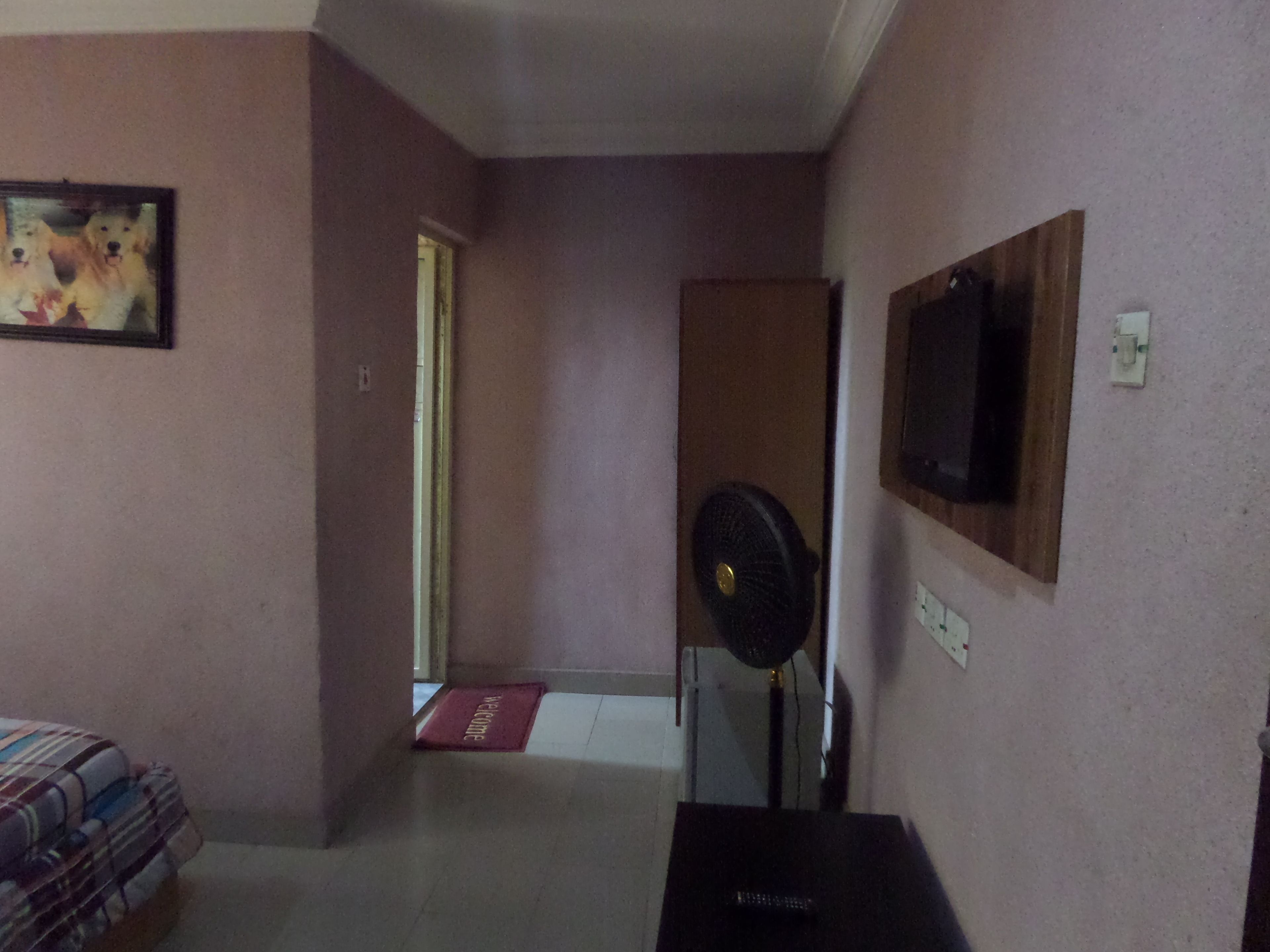 A room with a bed, a TV mounted on the wall, a fan, and a door leading to another room.