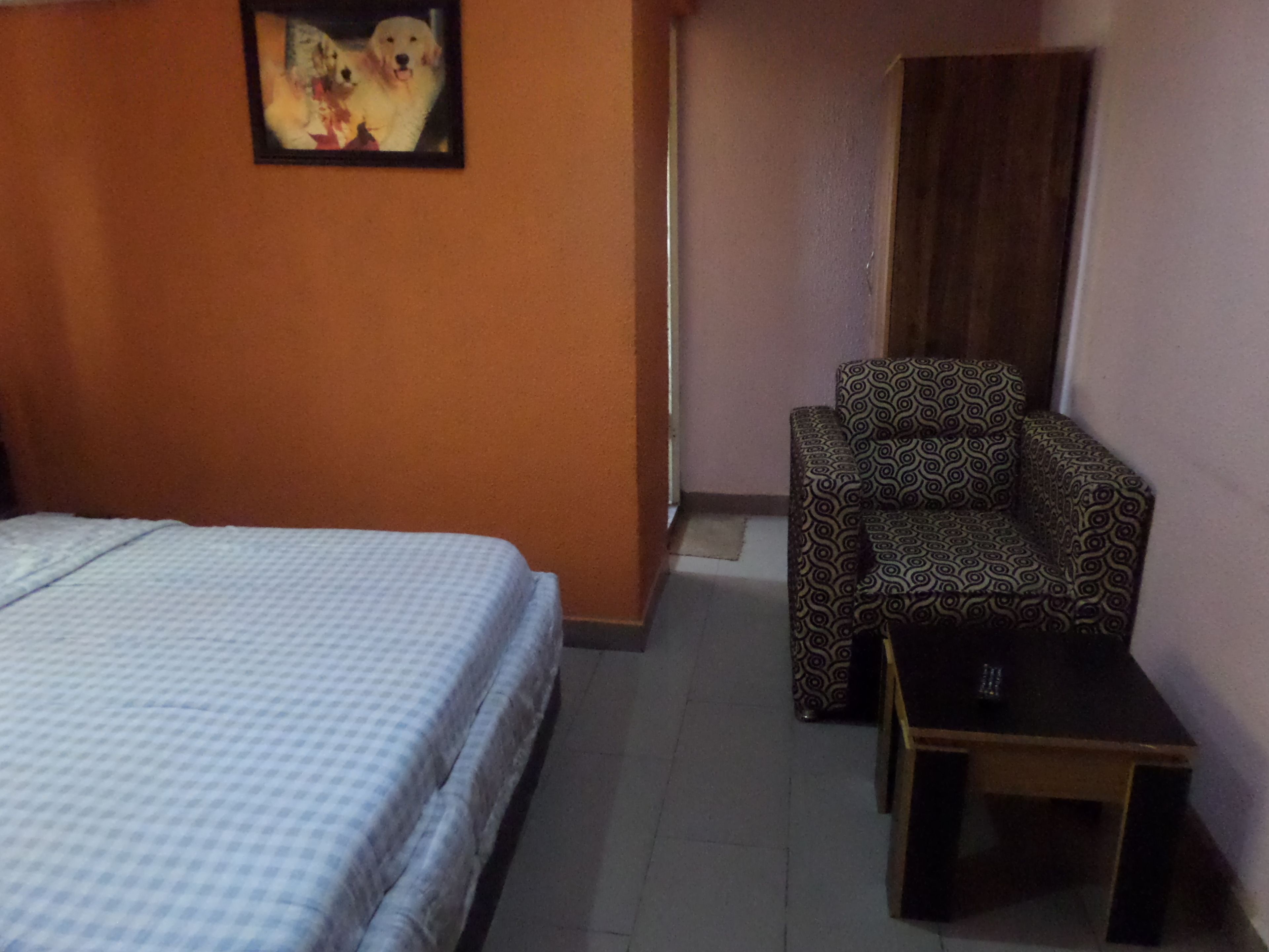 Ein Hotelzimmer mit einem Bett, einem gemusterten Sessel, einem kleinen Tisch und einem gerahmten Bild an der Wand.