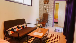 A cozy living room with a brown sofa, a small table with a vase, and a brick-patterned wall. - Lumut Cube Homestay Kontena (Lumut)