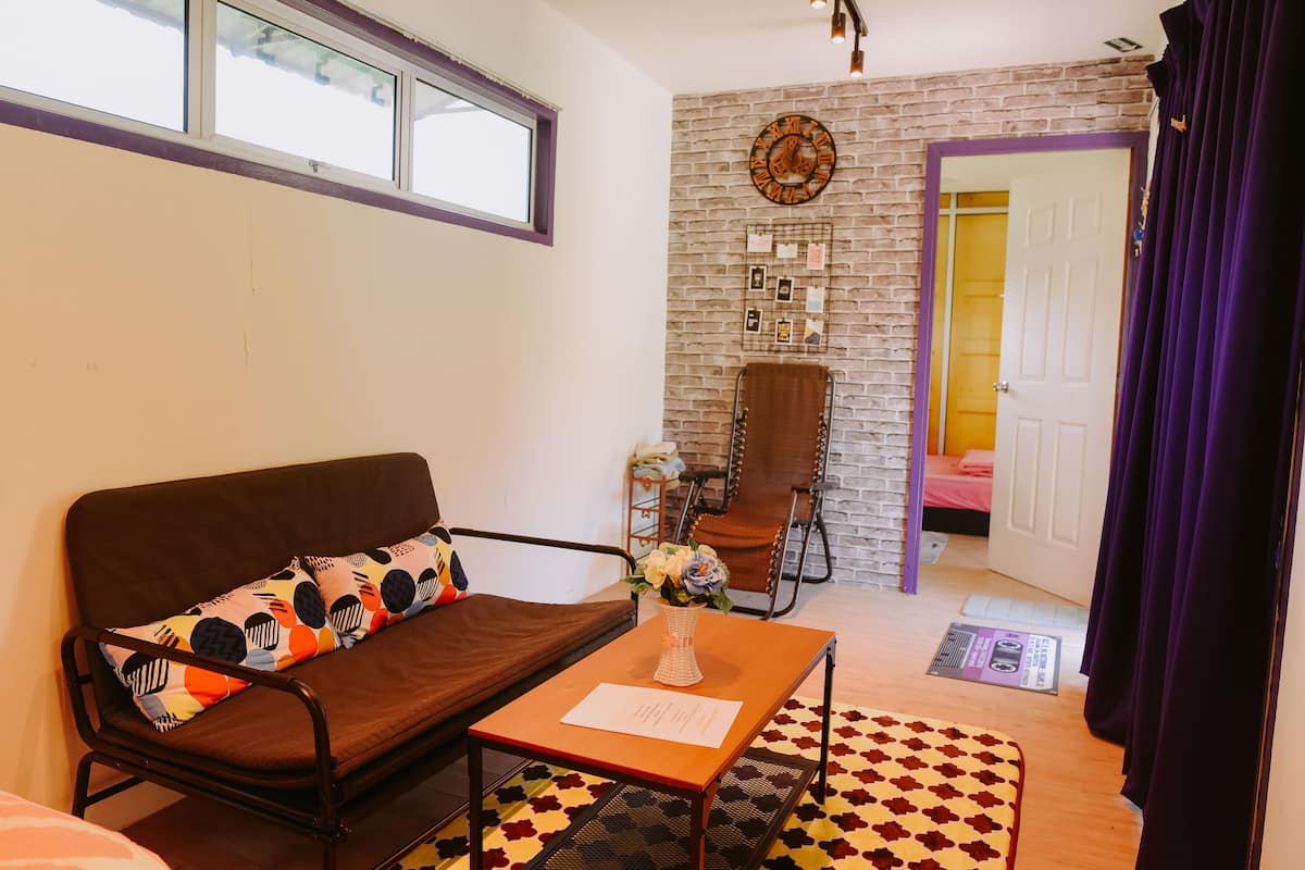 A cozy living room with a brown sofa, a small table with a vase, and a brick-patterned wall.