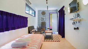 A compact hotel room with a bed, a small table, a chair, a TV, and an air conditioning unit. - Lumut Cube Homestay Kontena (Lumut)