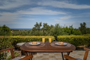 A wooden table with two plates of food and two glasses of orange juice, set against a backdrop of a garden and a clear sky.