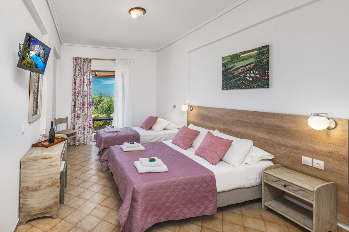 A hotel room with two beds, a TV, a painting, and a balcony with curtains.
