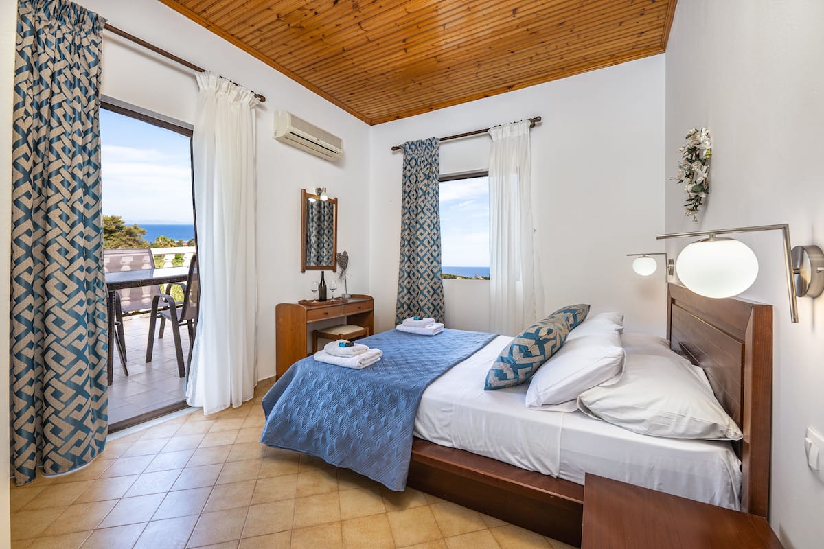 A bedroom with a bed, a desk, and a view of the sea.