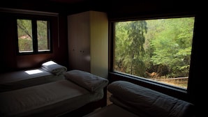 A bedroom with two beds, a wardrobe, and a large window offering a view of a forest.