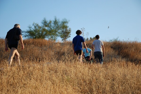 A group of people walking through a dry, grassy field with sparse trees in the background. - Jordan EcoPark (Waqqas)