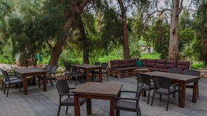 An outdoor patio area with wooden tables and chairs, a sofa, and a stone wall.