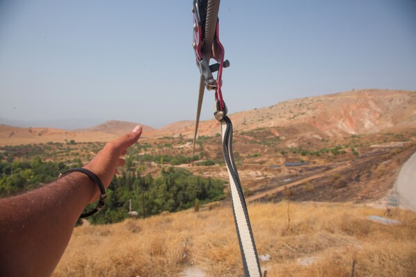 A hand holding a rope with a pulley system, set against a backdrop of a hilly landscape with sparse vegetation.