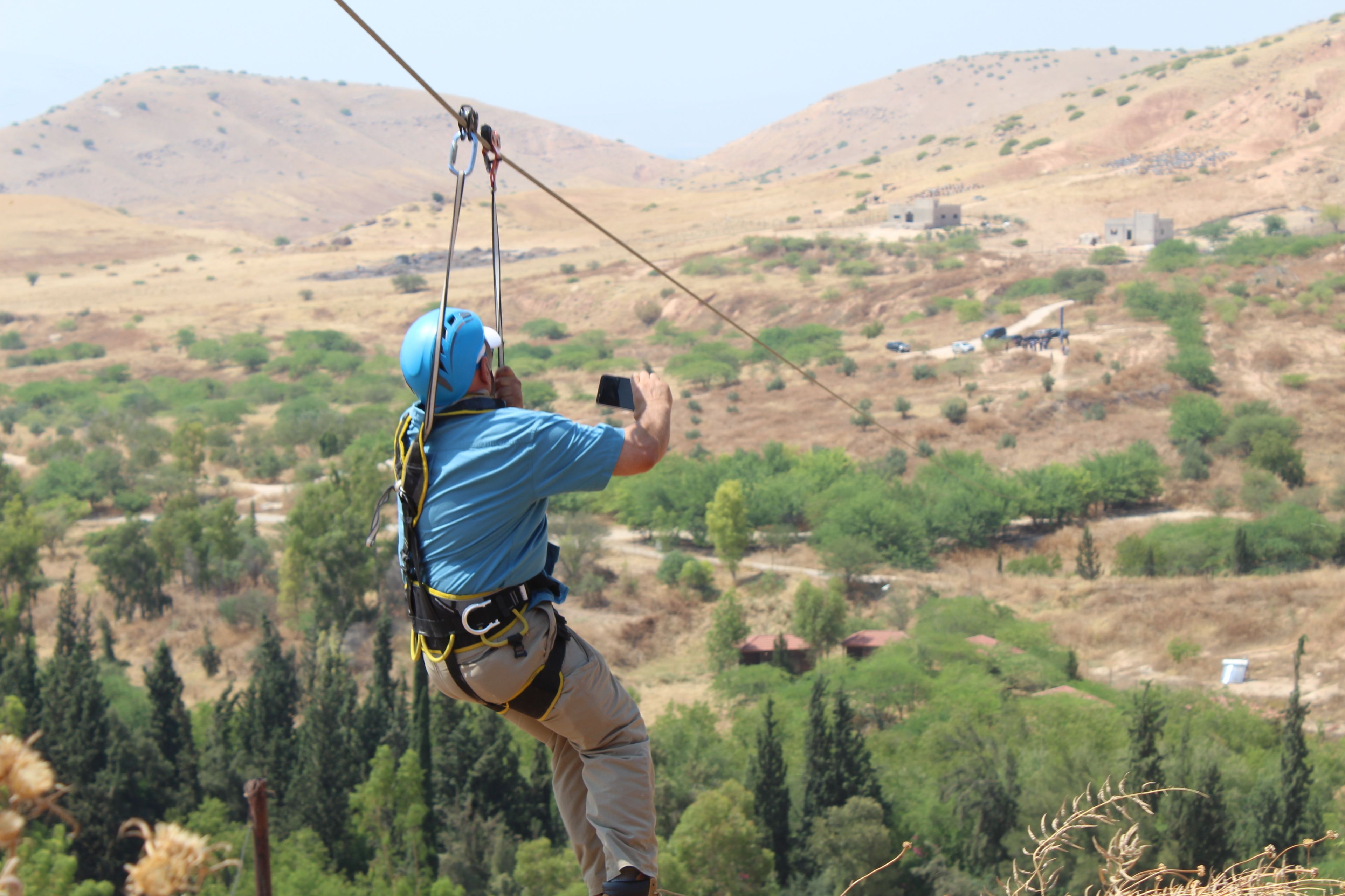 Una persona che sfreccia su una zip-line sopra un paesaggio collinare e scarsamente vegetato.
