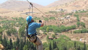 Una persona che sfreccia su una zip-line sopra un paesaggio collinare e scarsamente vegetato.