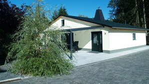 Ein kleines, eingeschossiges Gebäude mit dunklem Dach und weißer Fassade. Es hat eine grüne Tür und ein kleines Fenster an der Seite.