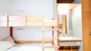 Un letto a castello con una scala in legno, un lavandino bianco e uno specchio in una stanza piccola.
