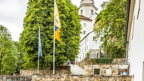 Un cortile con mura in pietra, tavoli e sedie in legno e bandiere.