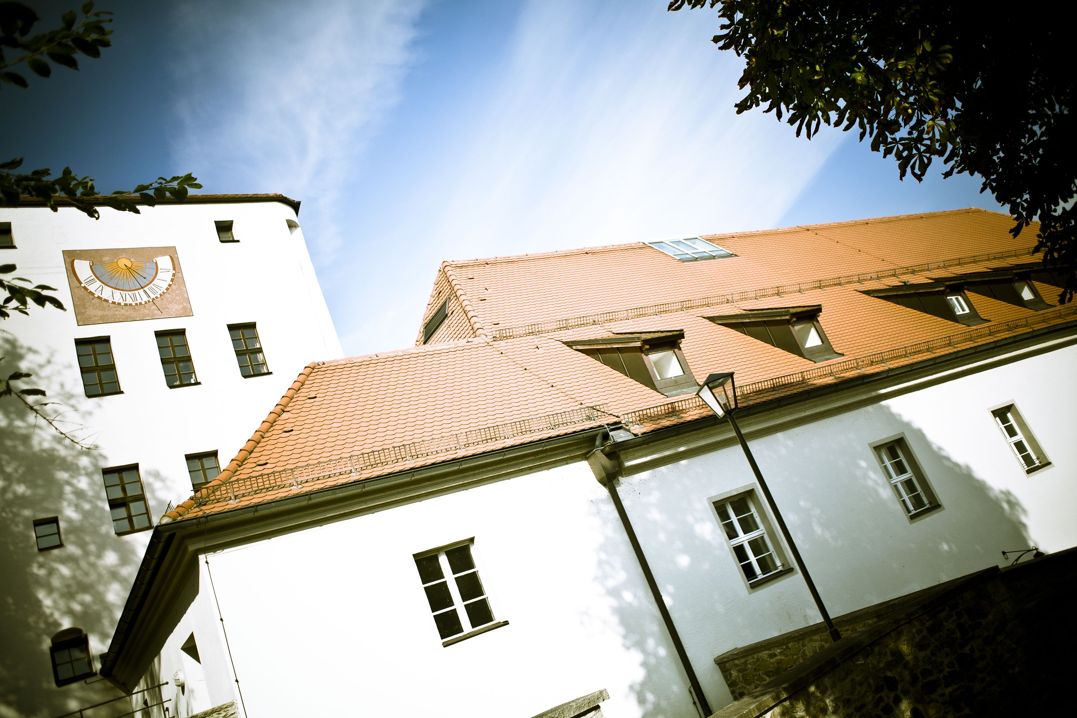 Um edifício com relógio na fachada, várias janelas e telhado de telhas.