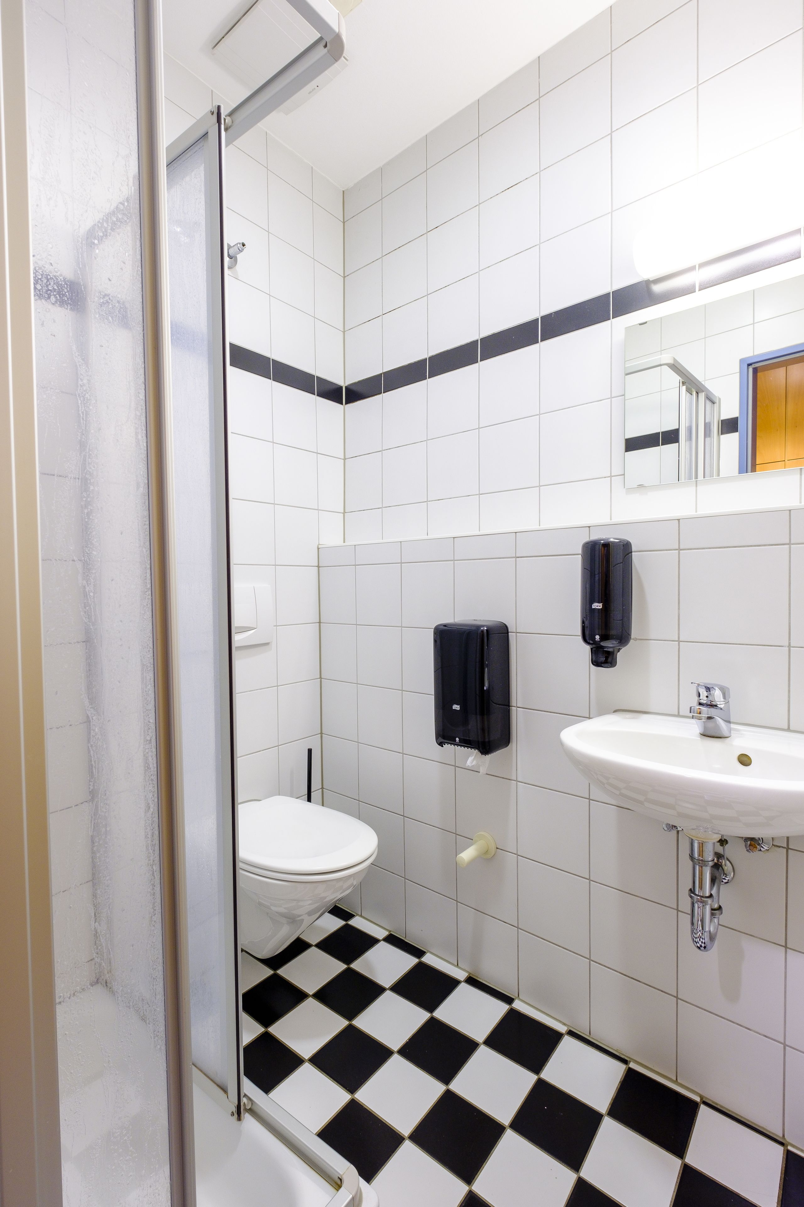 A bathroom with a glass shower door, a toilet, a sink, and two soap dispensers.