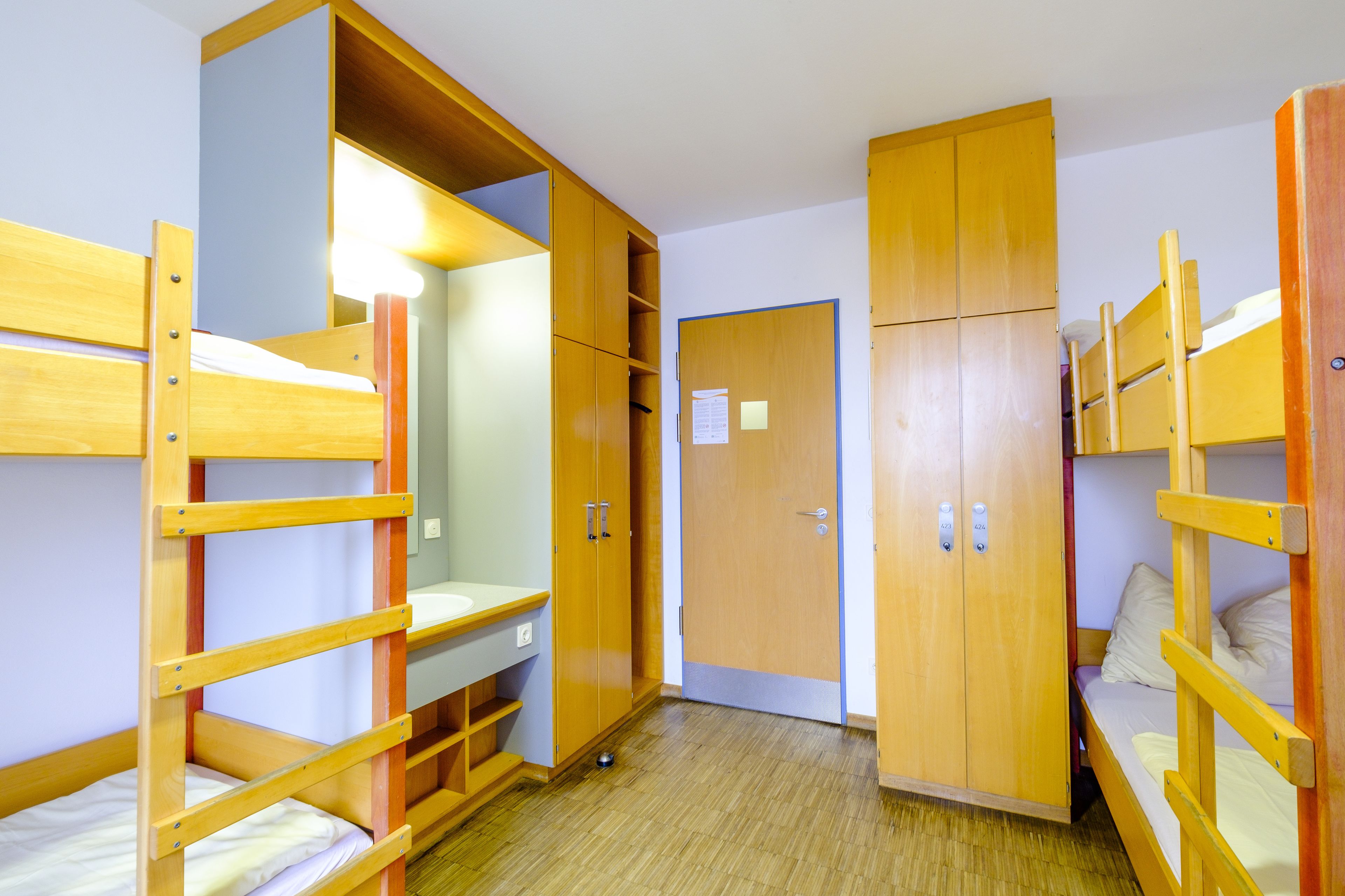 A dormitory room with bunk beds, wooden wardrobes, and a small desk area.