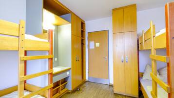 A dormitory room with bunk beds, wooden wardrobes, and a small desk area.