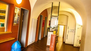 Un corridoio d'hotel con soffitti a volta, una reception e un cartello con la scritta 'Willkommen' (Benvenuti).