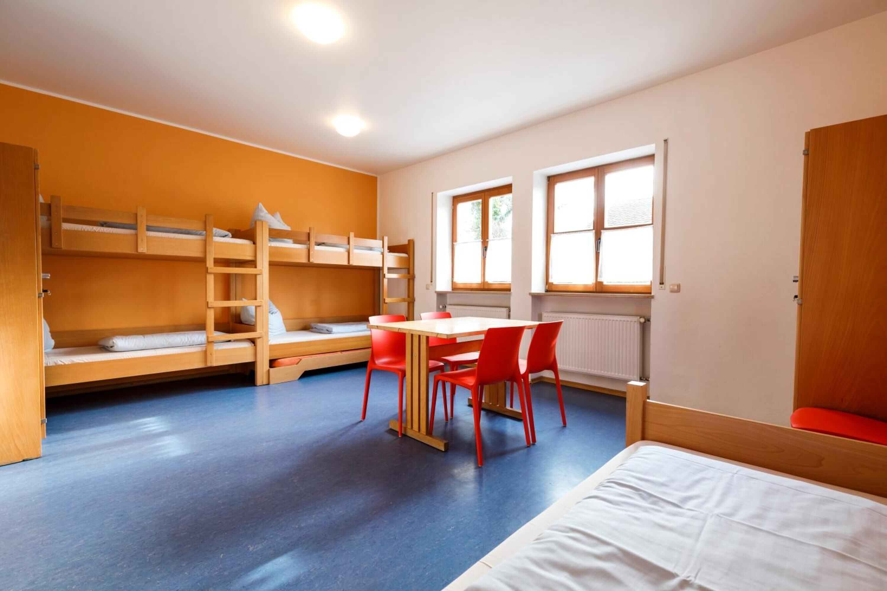 Un dormitorio con literas, una mesa de comedor con sillas y una ventana con persianas.