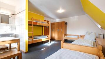 A dormitory room with bunk beds, a wooden table, a sink, and a wardrobe.