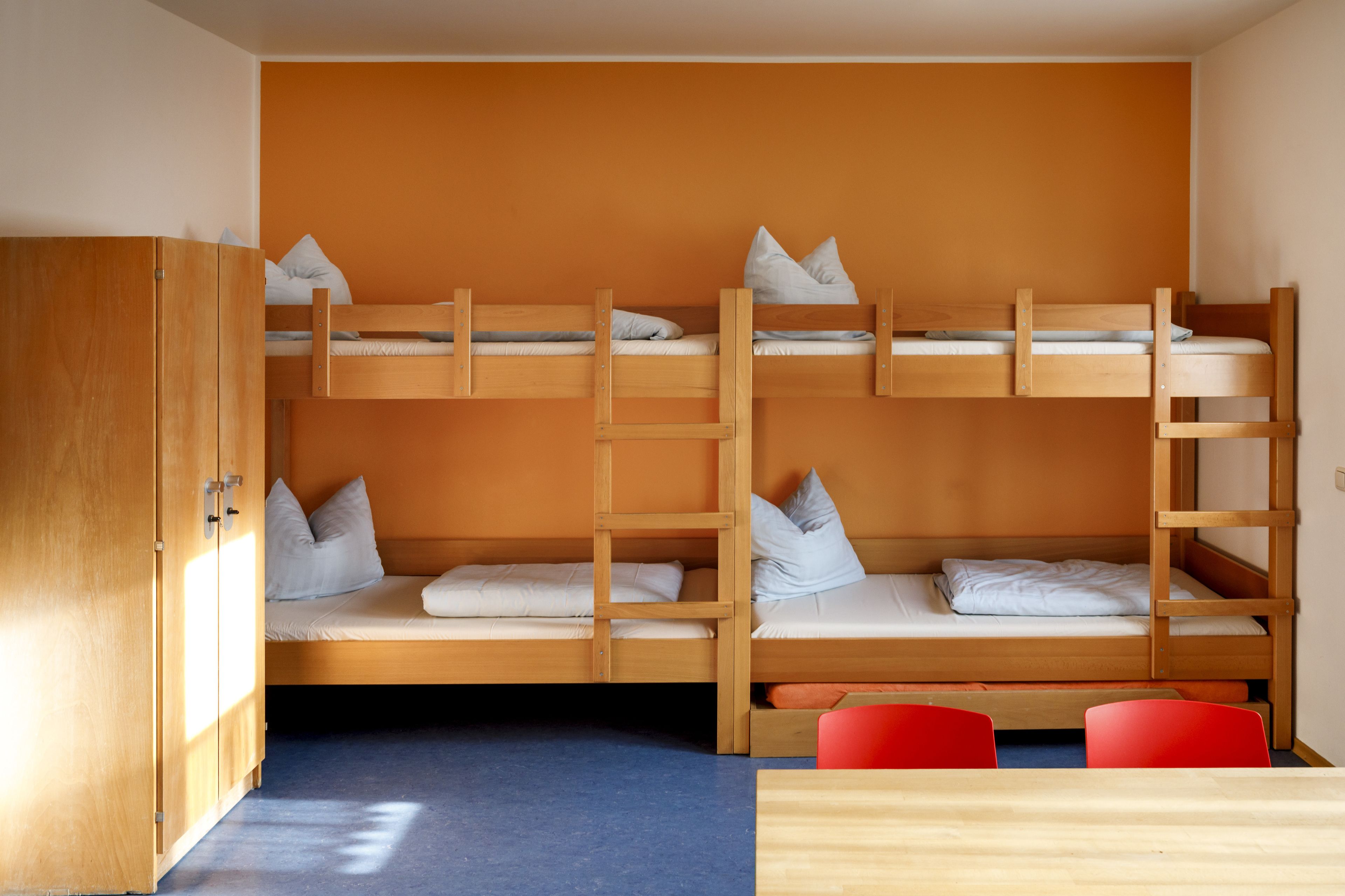 Une chambre avec un lit superposé, une armoire en bois et une table avec des chaises rouges.