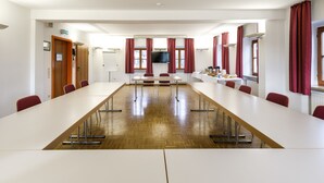 Ein Konferenzraum mit einem langen Tisch, roten Vorhängen und einem Fernseher an der Wand.