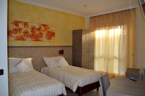 A hotel room with two beds, a brick accent wall, a large painting, a wardrobe, and a dining area with a table and chairs. - Locanda La Milanino (Cusano Milanino)