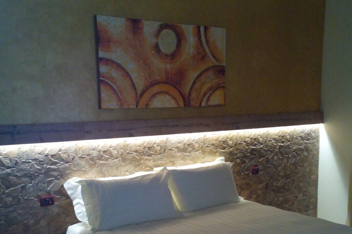 A bedroom with a stone headboard, a bed with white linens, and a small bedside table.