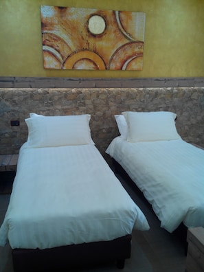 A room with two single beds, a stone wall, and a painting on the wall. - Locanda La Milanino (Cusano Milanino)