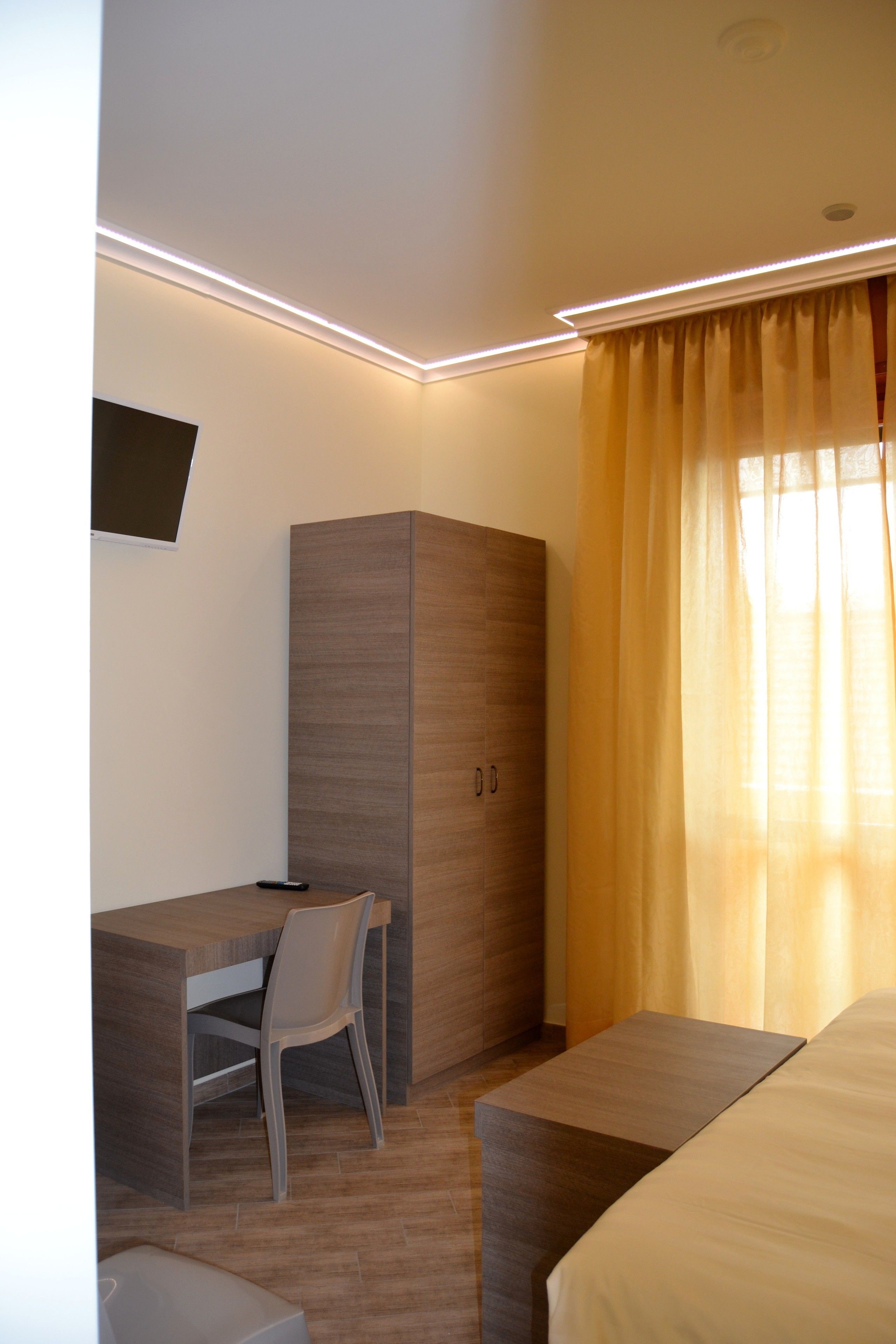 Une chambre d’hôtel moderne avec un bureau en bois, une chaise, une armoire et un lit.