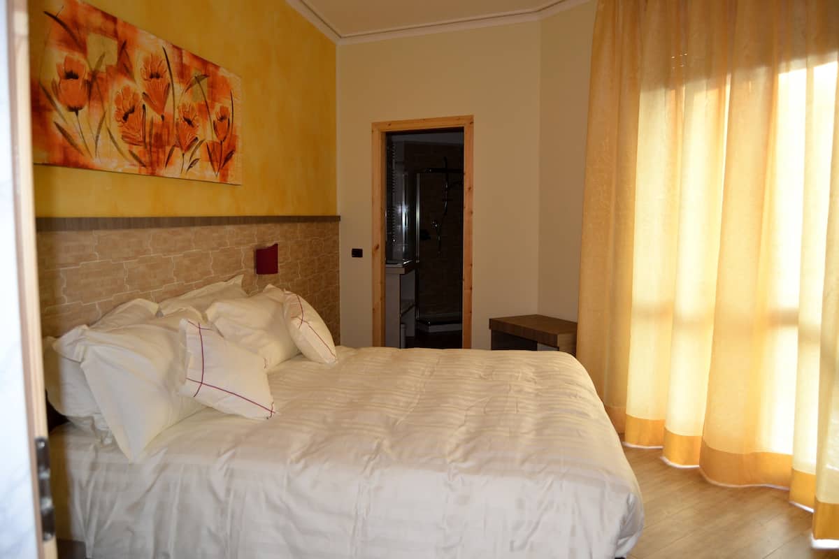 A bedroom with a large bed, a stone wall, a painting, and a bathroom door.
