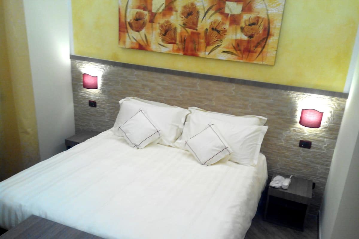 A neatly made bed with two pillows, a bedside table with a phone, and a wall-mounted light fixture.