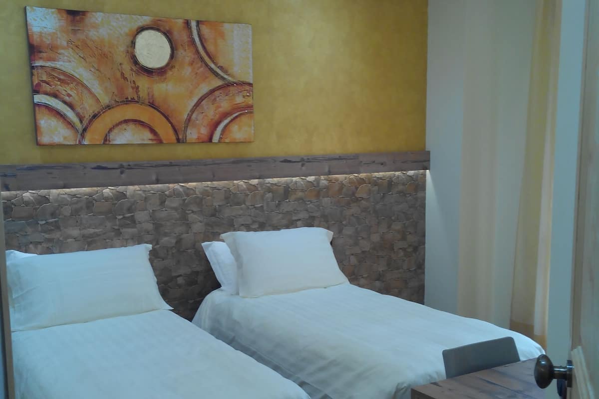 A room with two beds, a stone headboard, a wooden dresser, and a painting on the wall.