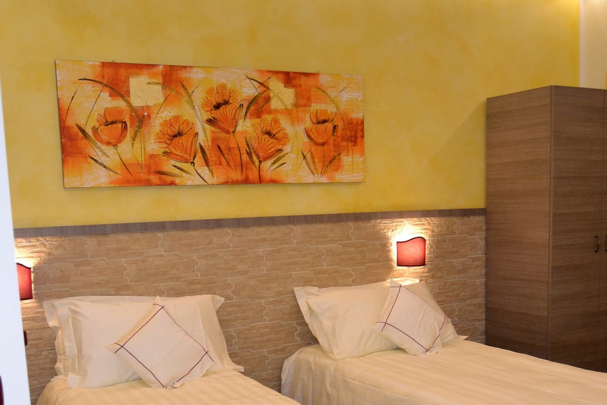 A hotel room with two beds, a wooden wardrobe, and a painting on the wall.
