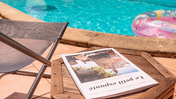 A wooden table with a magazine, a pool, and lounge chairs. - Chambre d'hôtes Agnes et Olivier (Burlats)