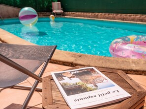 Une table en bois, un magazine, une piscine et des chaises longues.