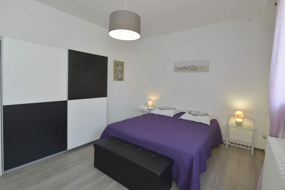 A modern bedroom with a bed, bedside tables, a bench, and artwork on the walls.