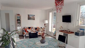 A modern living room with a sofa, a dining table with a patterned tablecloth, and a television. - Chambre d'hôtes Agnes et Olivier (Burlats)