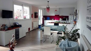 A modern kitchen with a dining area, a TV mounted on the wall, and a large window providing natural light. - Chambre d'hôtes Agnes et Olivier (Burlats)