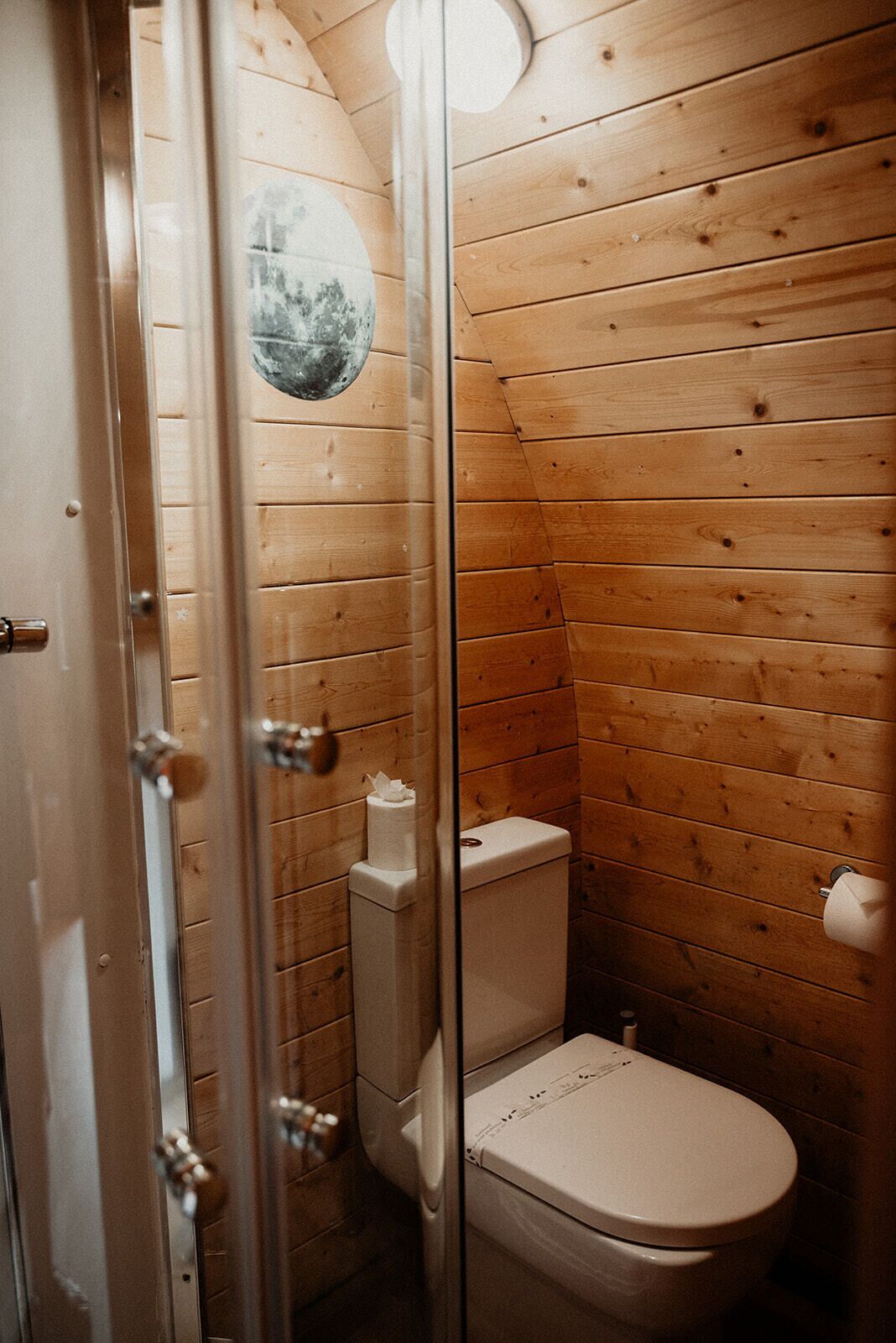 A wooden-paneled bathroom with a toilet, a glass shower enclosure, and a wooden door.