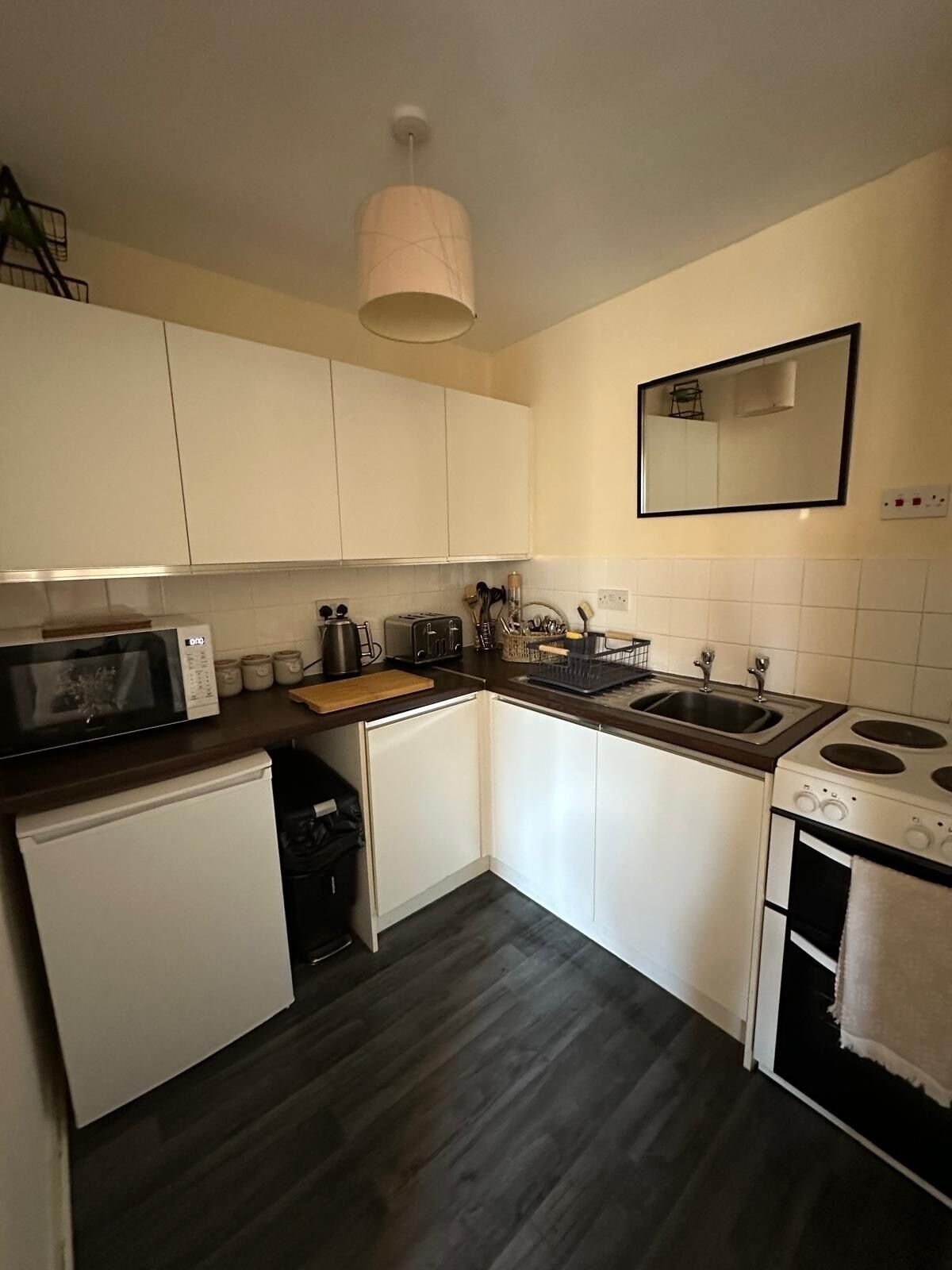 A compact kitchen with white cabinets, a microwave, a toaster, a sink, and a stove.