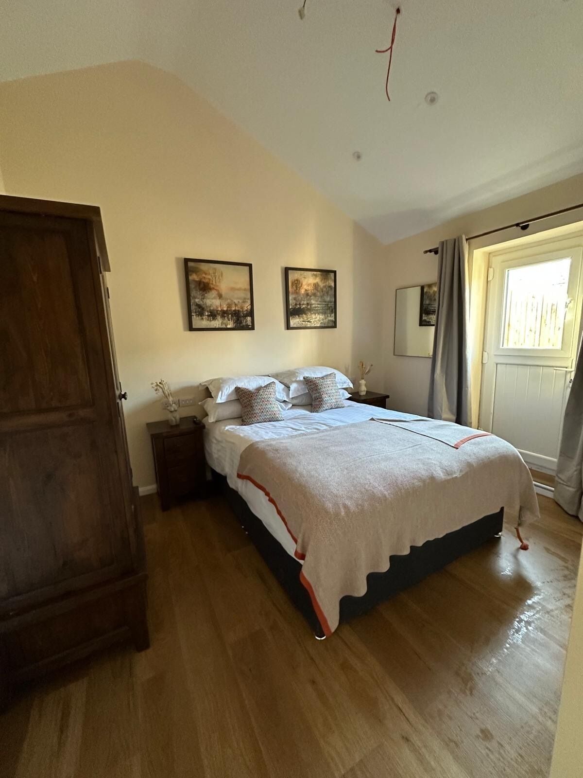 Un dormitorio con cama, armario de madera, dos cuadros y ventana con cortinas.