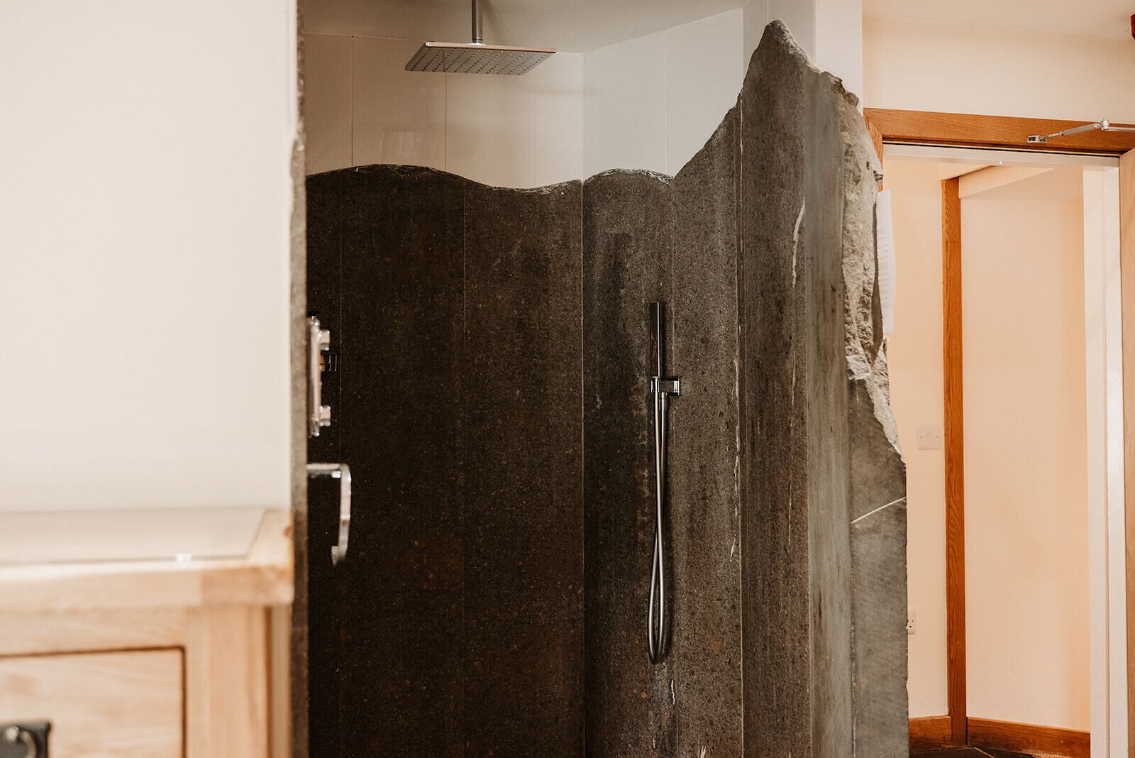 A shower enclosure with a dark, textured door and a handheld showerhead.