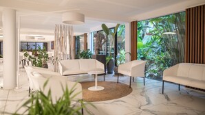 A modern lobby with white sofas, a round table, and a large window with tropical plants. - Ness By D-Ocean (Saint-Paul)