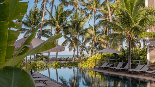 A poolside area with lounge chairs and umbrellas, surrounded by palm trees and a view of the ocean. - Ness By D-Ocean (Saint-Paul)