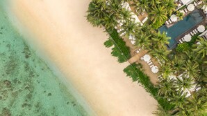 An aerial view of a beach resort with a pool area, palm trees, and a sandy beach. - Ness By D-Ocean (Saint-Paul)