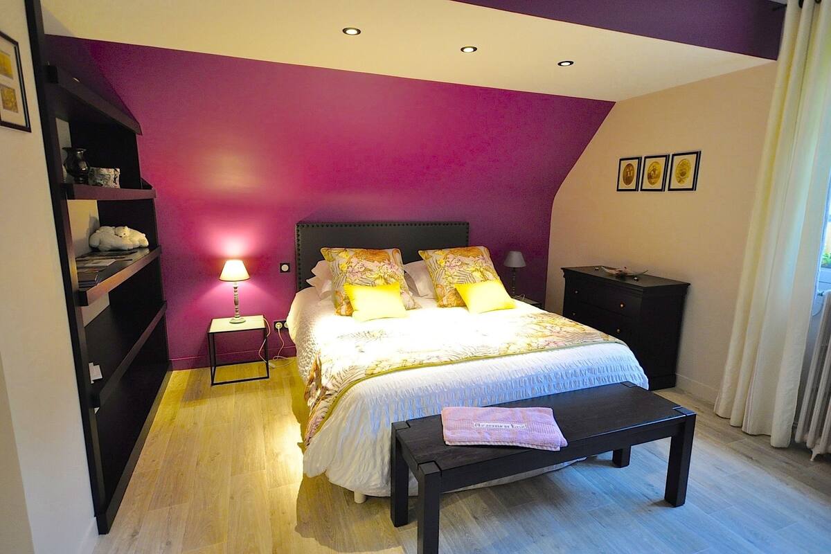Une chambre à coucher comprenant un lit, des tables de chevet, une commode, un banc et une fenêtre avec des rideaux.