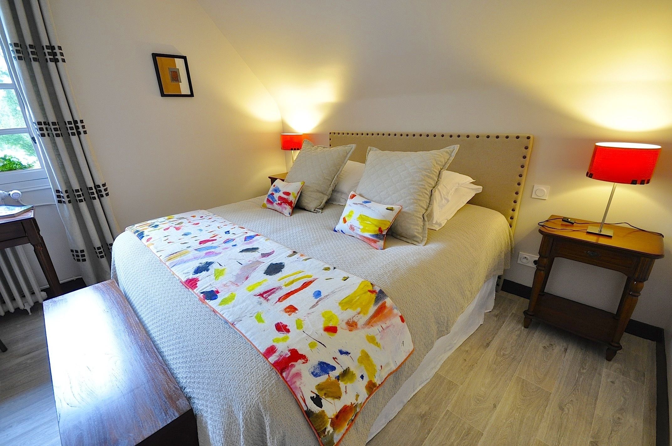 A neatly made bed with a colorful blanket, two bedside lamps, and a wooden nightstand.